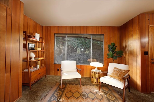 living area featuring wood walls and dark carpet