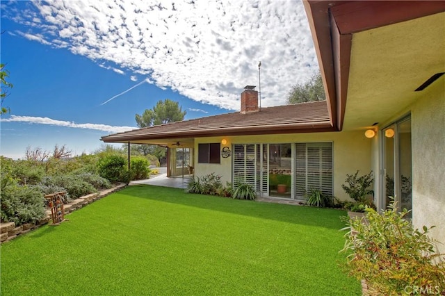 back of house featuring a chimney, a lawn, a patio area, and stucco siding