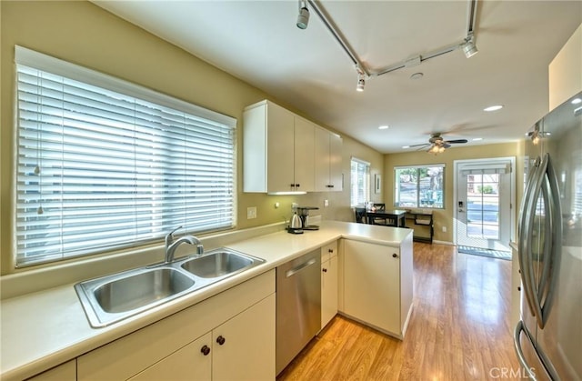 kitchen with white cabinets, a peninsula, stainless steel appliances, light countertops, and a sink