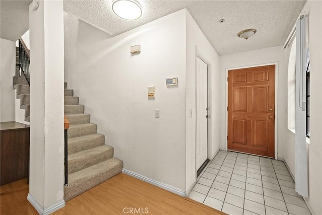 entryway featuring light tile patterned floors, a textured ceiling, baseboards, and stairs