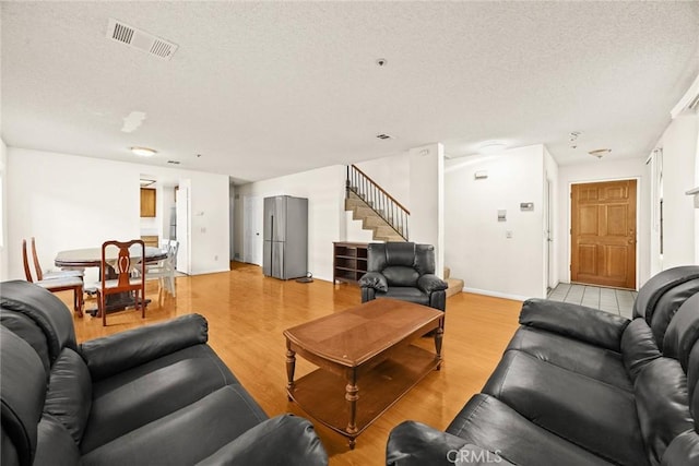 living area with baseboards, visible vents, light wood-style flooring, stairs, and a textured ceiling