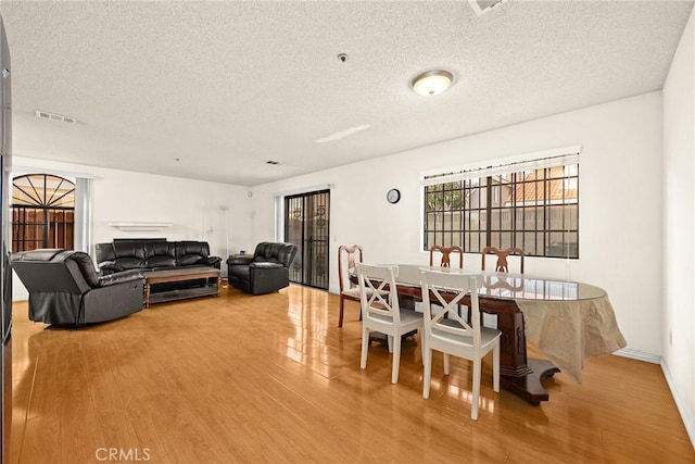 dining space with a textured ceiling, wood finished floors, and visible vents