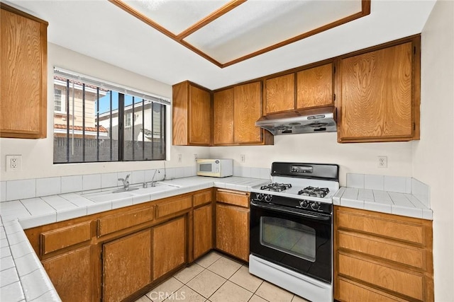 kitchen with white microwave, under cabinet range hood, a sink, brown cabinets, and gas range oven