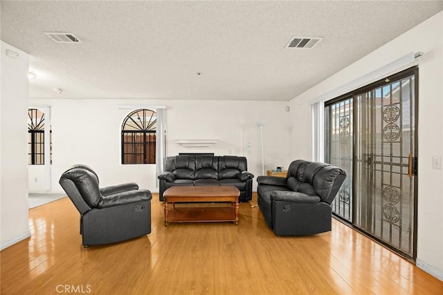 living room with light wood-style floors, baseboards, visible vents, and a textured ceiling