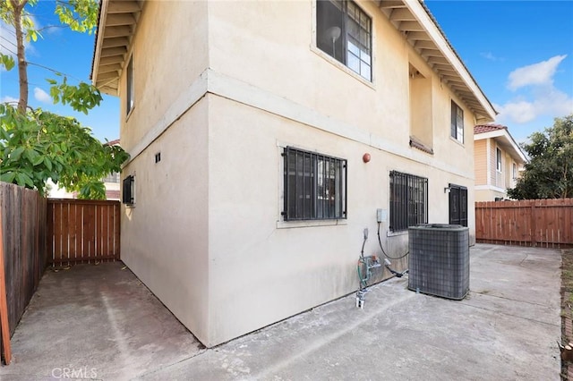 view of side of home featuring central air condition unit, a fenced backyard, a patio, and stucco siding