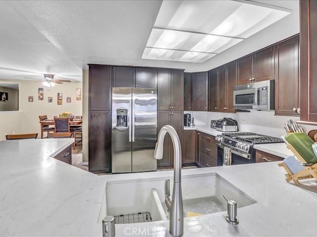 kitchen featuring stainless steel appliances, dark brown cabinets, a sink, and a ceiling fan