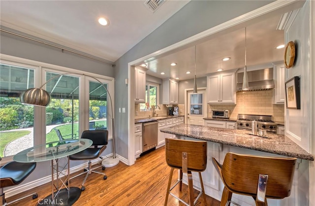 kitchen with visible vents, white cabinetry, wall chimney range hood, appliances with stainless steel finishes, and light stone countertops