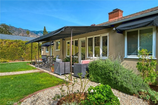 back of house with a mountain view, a yard, stucco siding, a chimney, and a patio area