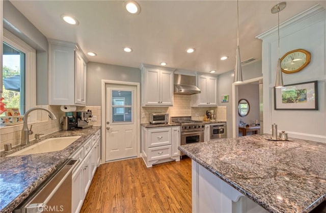 kitchen with pendant lighting, stainless steel appliances, white cabinetry, a sink, and wall chimney range hood