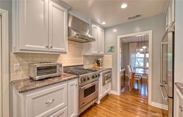 kitchen with a toaster, visible vents, high quality appliances, white cabinetry, and wall chimney range hood