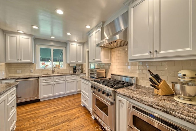 kitchen with white cabinets, appliances with stainless steel finishes, light wood-style floors, a sink, and exhaust hood