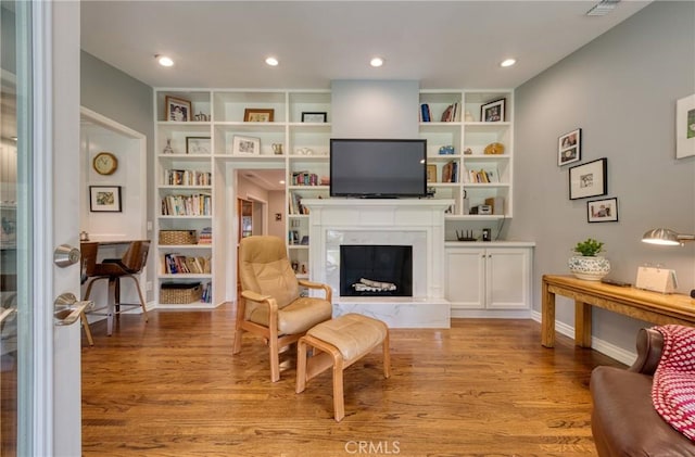 sitting room featuring baseboards, light wood-type flooring, built in shelves, a fireplace, and recessed lighting