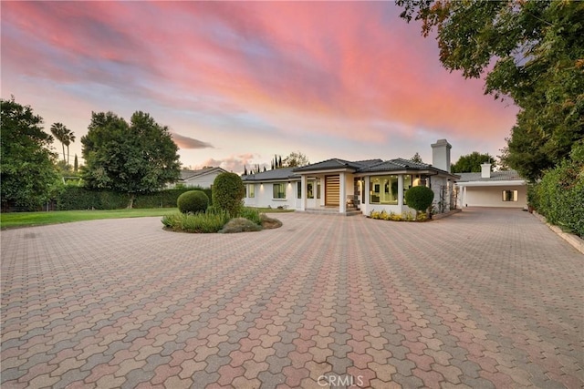 view of front of home with a chimney, curved driveway, and stucco siding