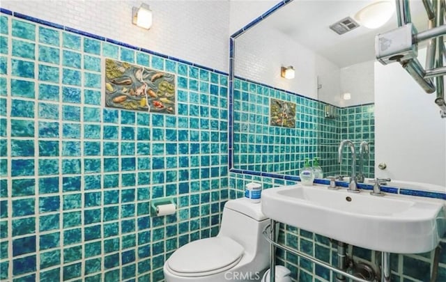 half bath with toilet, a sink, visible vents, and tile walls