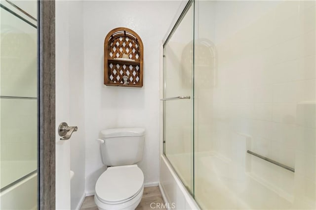 bathroom featuring baseboards, shower / bath combination with glass door, and toilet