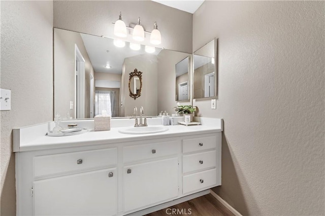 bathroom with a textured wall, vanity, baseboards, and wood finished floors