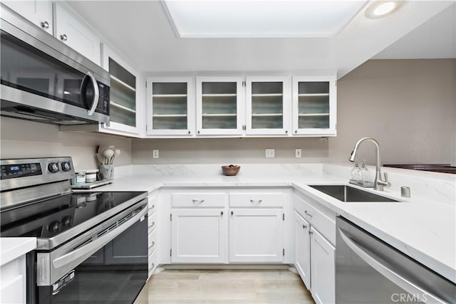 kitchen with appliances with stainless steel finishes, white cabinets, a sink, and glass insert cabinets