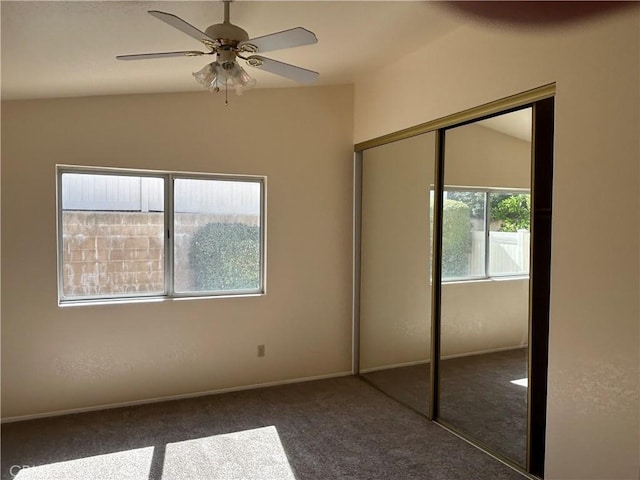 unfurnished bedroom with dark colored carpet, a closet, a ceiling fan, and baseboards