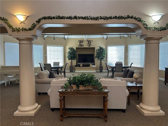 carpeted living room featuring arched walkways, beam ceiling, decorative columns, and baseboards