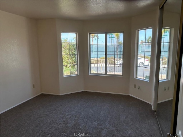 empty room with a healthy amount of sunlight, baseboards, dark carpet, and a textured ceiling