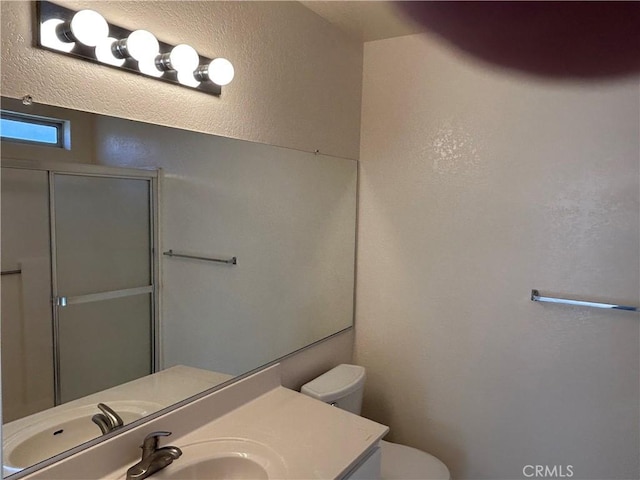 full bath featuring a textured wall, vanity, a shower with door, and toilet