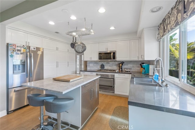 kitchen featuring light wood finished floors, decorative backsplash, appliances with stainless steel finishes, white cabinets, and a sink