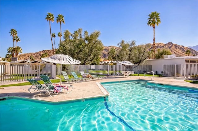 community pool with a patio area, fence, and a mountain view