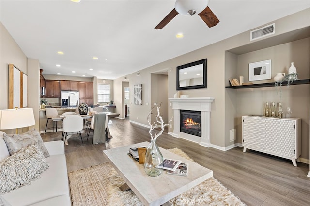 living room with baseboards, visible vents, a glass covered fireplace, dark wood-style floors, and recessed lighting