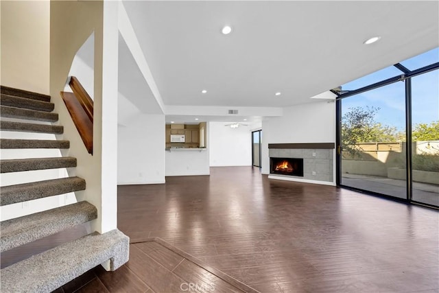 unfurnished living room with recessed lighting, dark wood-type flooring, a lit fireplace, stairway, and a wall of windows