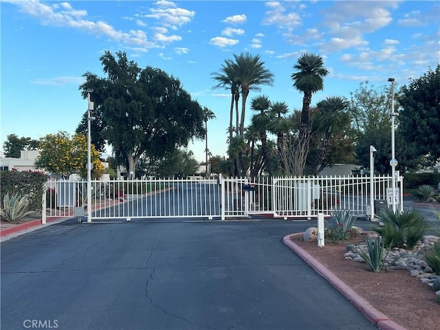 view of street with a gate, a gated entry, street lights, and curbs