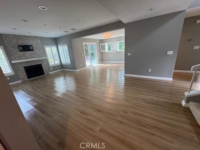 unfurnished living room featuring recessed lighting, dark wood-style flooring, a stone fireplace, and baseboards