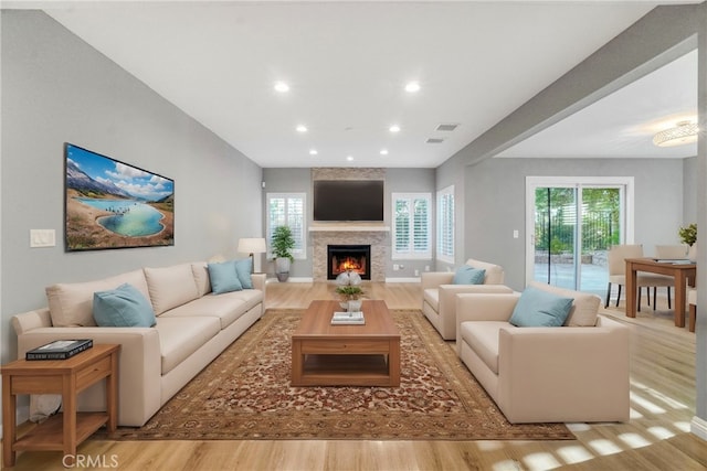 living area with recessed lighting, a warm lit fireplace, baseboards, and wood finished floors