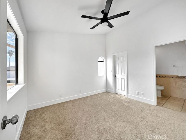unfurnished bedroom with carpet flooring, ceiling fan, baseboards, vaulted ceiling, and ensuite bath