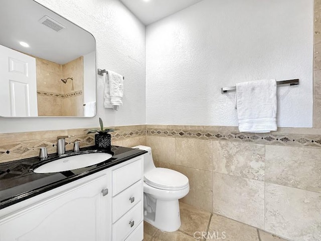 full bath with a tile shower, tile walls, toilet, vanity, and visible vents