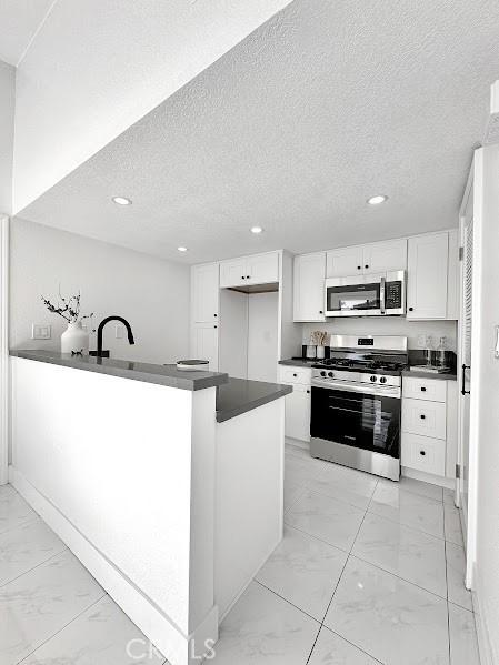 kitchen with marble finish floor, dark countertops, a textured ceiling, white cabinets, and appliances with stainless steel finishes