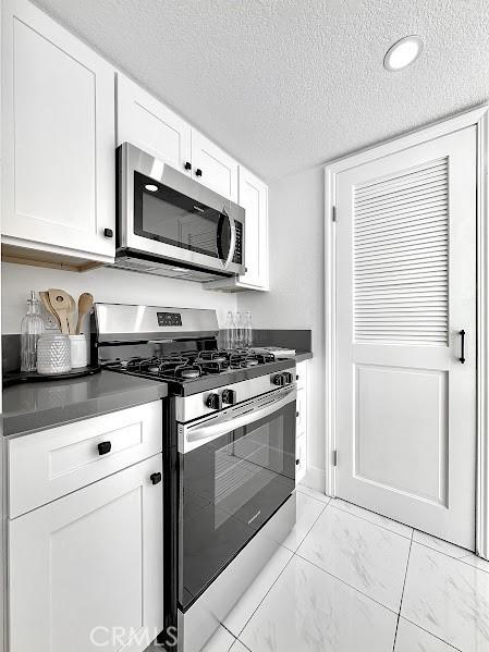 kitchen with appliances with stainless steel finishes, a textured ceiling, white cabinetry, and dark countertops