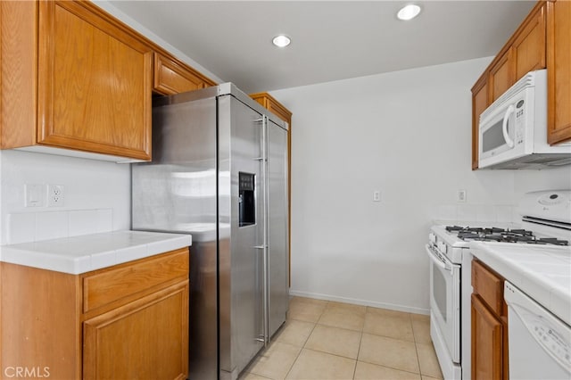 kitchen with tile countertops, white appliances, brown cabinetry, and light tile patterned flooring