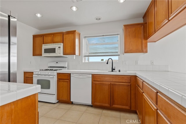 kitchen featuring white appliances, tile counters, brown cabinets, and a sink