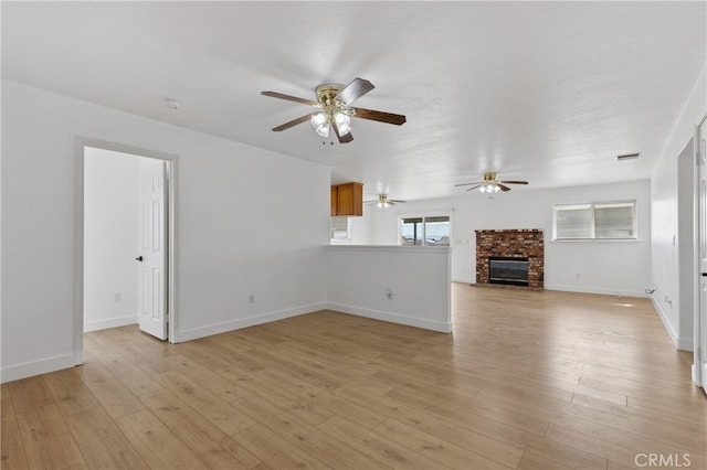 unfurnished living room featuring light wood finished floors, a brick fireplace, visible vents, and baseboards