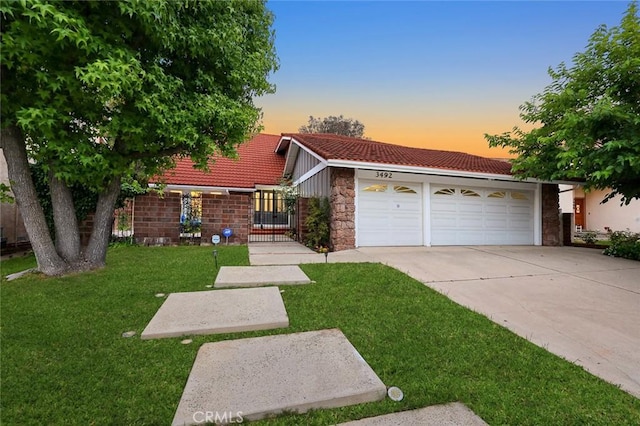 view of front of property featuring a garage, concrete driveway, a tiled roof, a yard, and stone siding