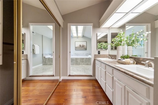 interior space featuring vaulted ceiling with skylight, a sink, and wood finished floors