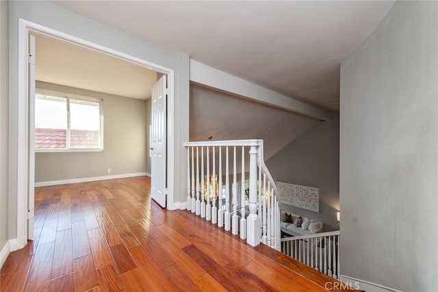 corridor with baseboards, wood finished floors, and an upstairs landing