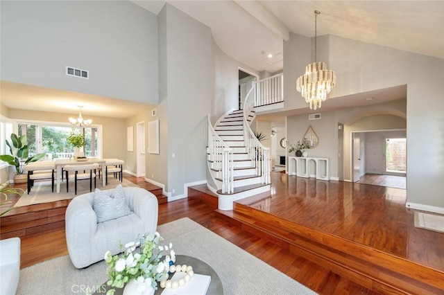 living room featuring visible vents, an inviting chandelier, wood finished floors, baseboards, and stairs