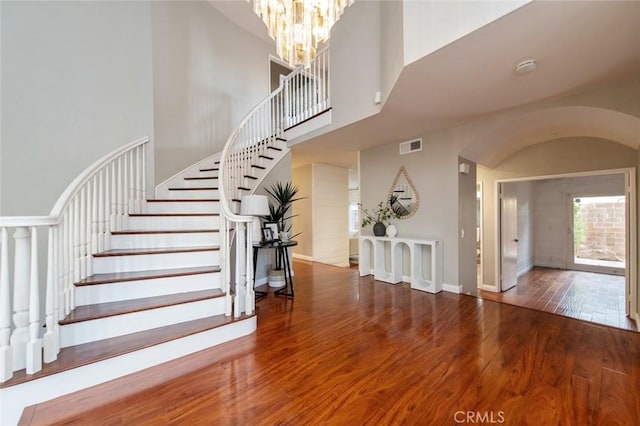 entrance foyer with a towering ceiling, stairs, arched walkways, and wood finished floors