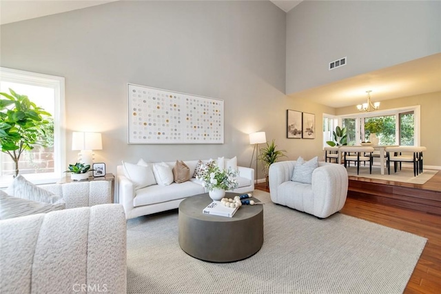 living room with visible vents, a notable chandelier, a towering ceiling, and wood finished floors