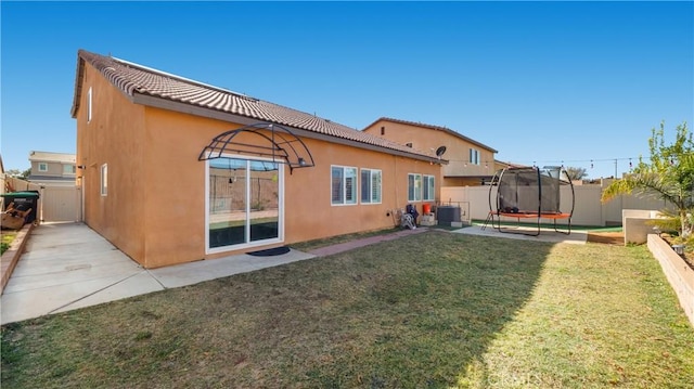 rear view of house with a trampoline, stucco siding, a lawn, fence, and cooling unit