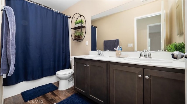 bathroom featuring double vanity, toilet, a sink, and wood finished floors