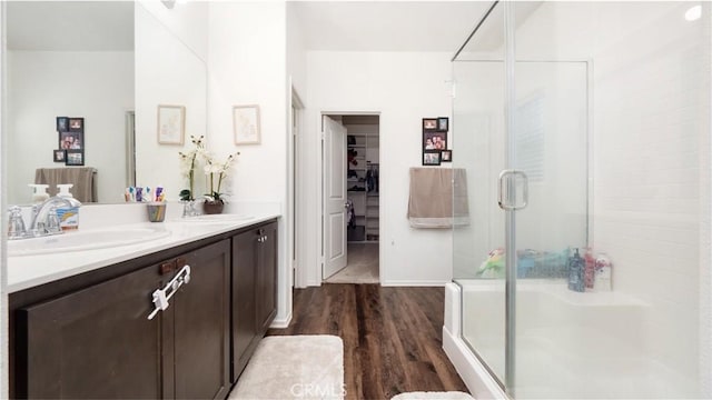 bathroom featuring double vanity, a stall shower, a sink, and wood finished floors