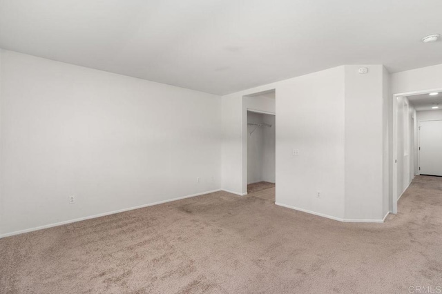 unfurnished bedroom featuring baseboards, a spacious closet, and light colored carpet