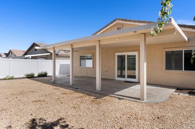 rear view of property featuring a patio area, fence, and stucco siding